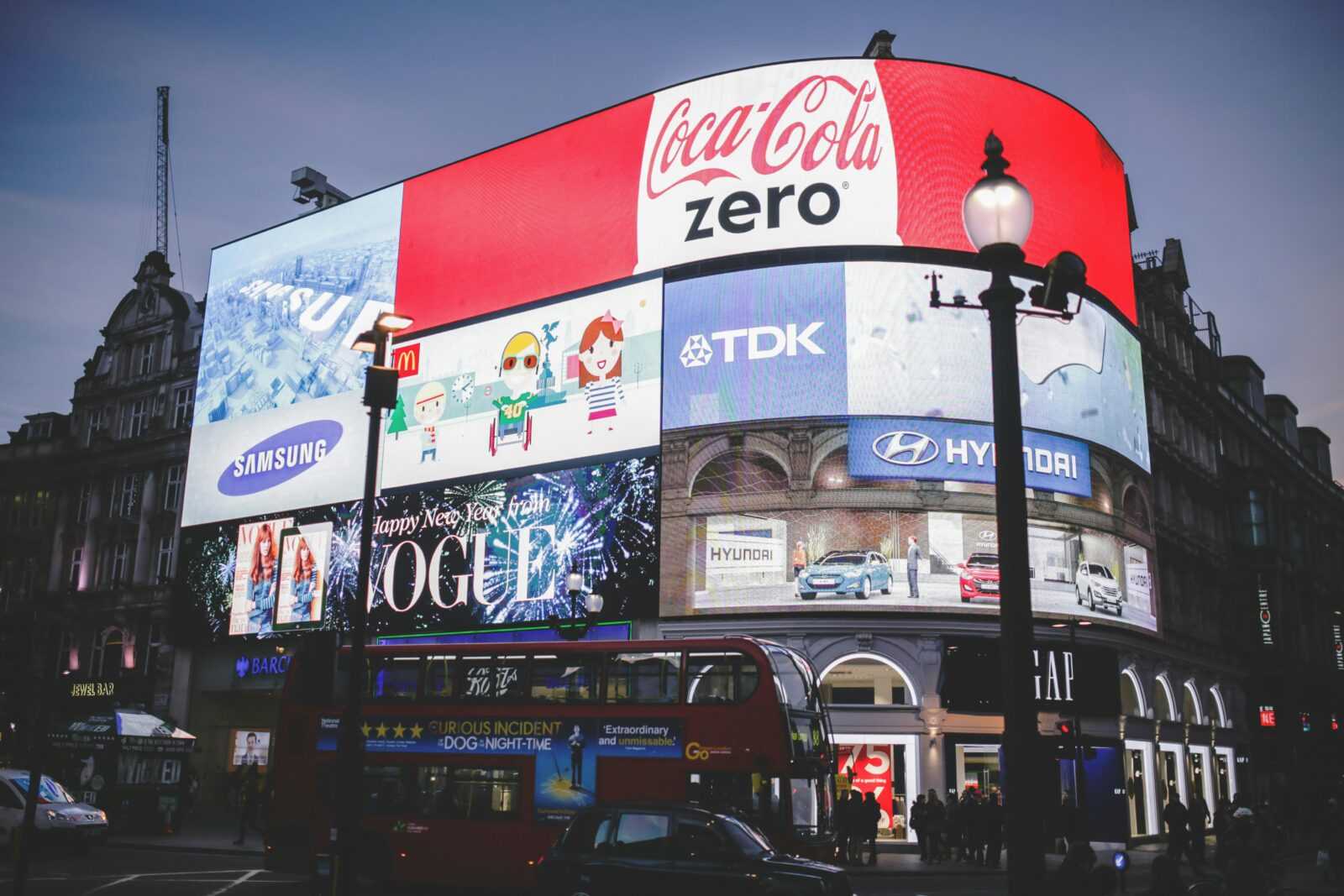 Night view of Piccadilly Circus in London with bright billboards and a red double-decker bus.