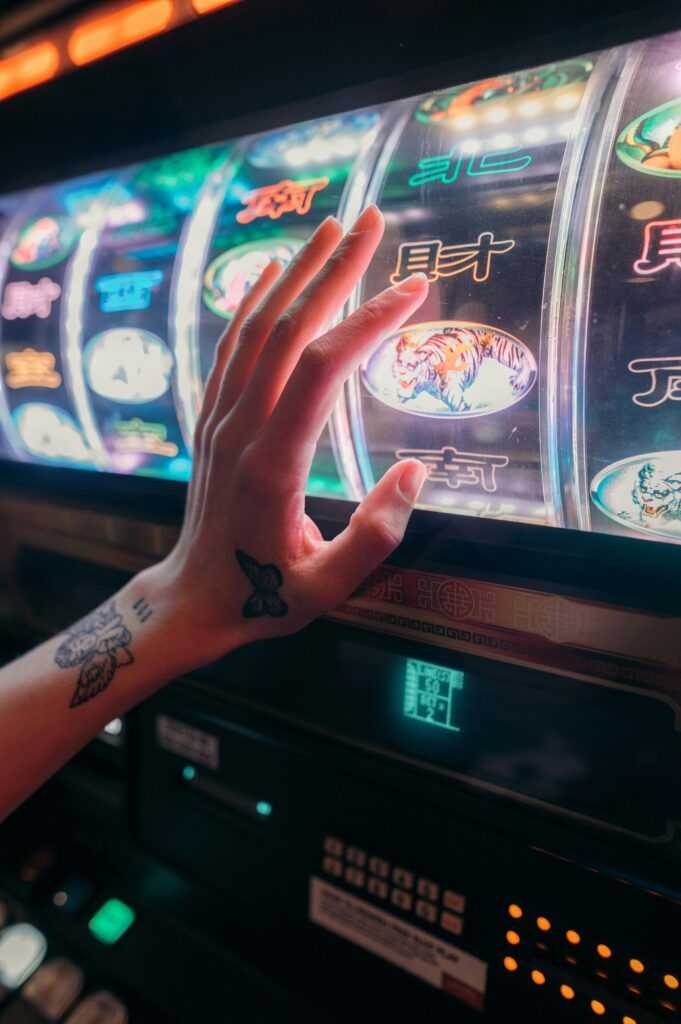 Tattooed hand playing slot machine in vibrant casino setting, emphasizing chance and excitement.