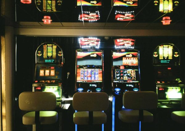 Slot machines in a dimly lit casino with reflective ceiling and empty chairs.